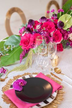 the table is set with pink and purple flowers, gold place settings, and black plates