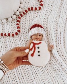 a person holding a snowman ornament in front of a white knitted blanket