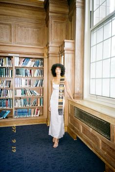 a woman standing in front of a bookshelf holding a skateboard