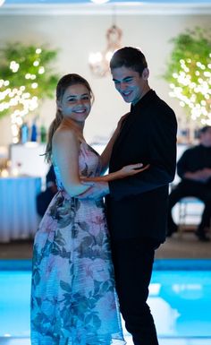 a man and woman standing next to each other in front of a pool at night