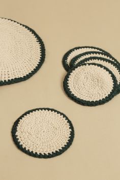 four black and white crocheted coasters on a beige tablecloth with green trim