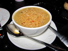 a bowl of food sitting on top of a white plate next to spoons and utensils