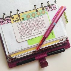 a pink pen sitting on top of a notebook with a calendar in the middle and writing numbers