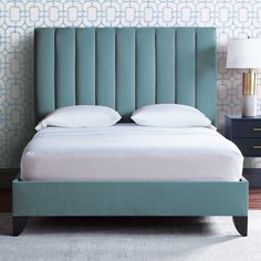 a blue bed with two pillows on top of it and a night stand next to it