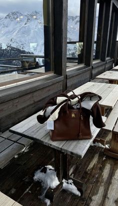 a brown purse sitting on top of a wooden bench next to a window with mountains in the background