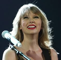 a woman holding a microphone in her right hand and singing into the microphone on stage