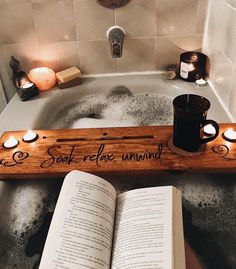 an open book sitting on top of a bath tub next to candles and a candle holder