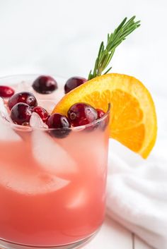 a drink with orange slices and cranberries on the rim, garnished with rosemary