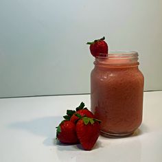 two strawberries sit next to a jar of smoothie