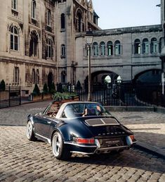 a car parked in front of a large building on a cobblestone road next to a fence