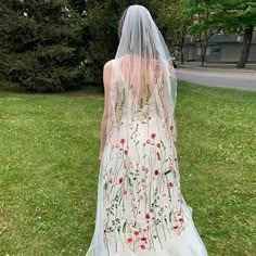 the back of a bride's wedding dress with flowers on it, walking in grass