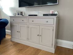 a flat screen tv mounted on top of a white cabinet next to a blue chair