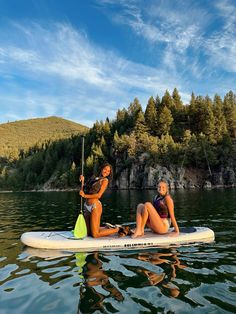 two women are sitting on a paddle board in the water