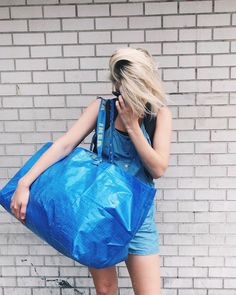 a woman in overalls is holding a blue bag and talking on her cell phone