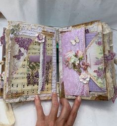 a hand is holding an open book with flowers and laces on it, while the pages have been altered