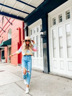 a woman in ripped jeans and a hat is walking down the street with her arms outstretched