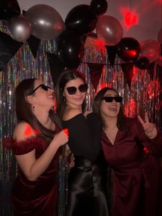 three women standing next to each other in front of balloons and streamers at a party