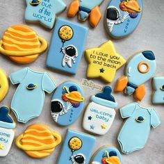 cookies decorated to look like baby's clothes and space related items are arranged on a table