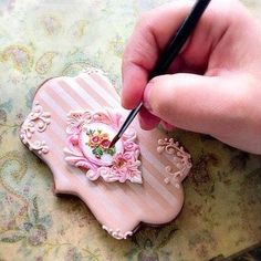 a hand is holding a pen and writing on a heart shaped brooch with flowers