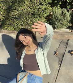 a woman standing on the side walk with her hand up in the air while wearing jeans and a crop top