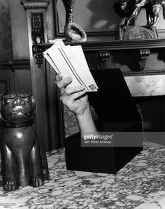 a black and white photo of a person's hand holding up some paper in front of a cat figurine