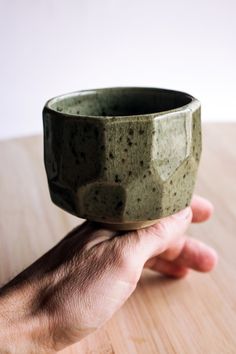 a hand holding a green bowl on top of a wooden table