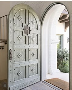 an arched doorway with wooden flooring and white painted doors, leading into a courtyard