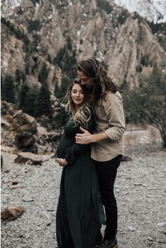 a man and woman hugging each other in the mountains