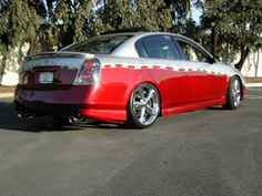 a red and silver car parked in a parking lot next to some trees on a sunny day