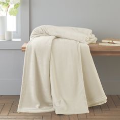 a white blanket sitting on top of a wooden table next to a vase with flowers