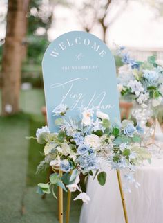 a welcome sign sitting on top of a table next to a white and blue flower arrangement