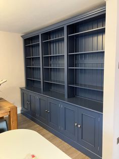 an empty room with blue bookcases and a wooden table in the corner,