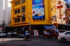 a busy city street filled with lots of cars and people riding bikes in front of a yellow building