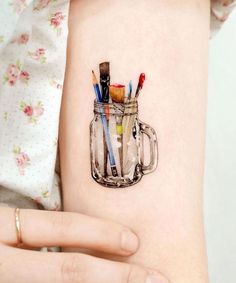 a woman's arm with a jar filled with paint brushes and pencils on it