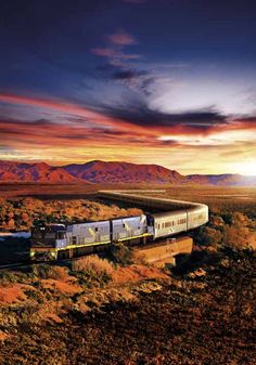 a train is traveling through the desert with mountains in the backgrouds at sunset