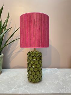 a green table lamp sitting on top of a counter next to a potted plant