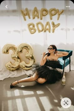 a woman in a black dress sitting on a blue chair with the number 35 balloon behind her