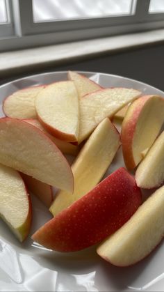 sliced apples on a white plate next to a window