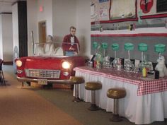 an old car is parked in the middle of a room with tables and stools