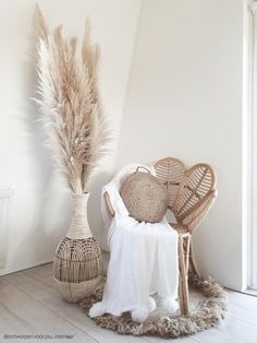 a wicker chair next to a vase with pamodia in it on a white floor