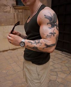 a man with tattoos on his arm holding an object in one hand and looking at the camera