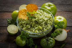 a bowl filled with rice next to green apples and limes on top of a wooden table