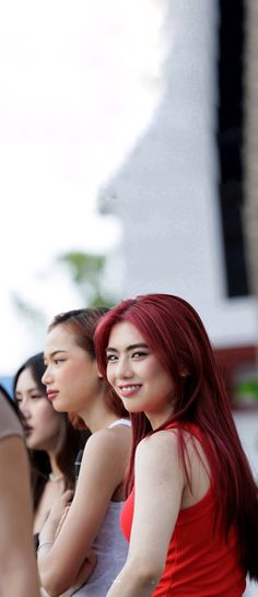 three young women standing next to each other in front of a building and one woman with red hair