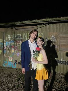 a man and woman standing next to each other in front of a wall with graffiti on it