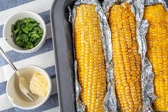 corn on the cob in foil with butter and spinach leaves next to it