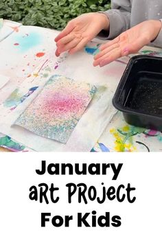 a child's hands on top of a table with paint and paper in front of it