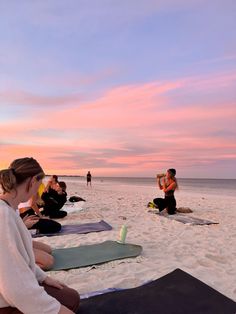 a group of people sitting on top of a beach next to the ocean at sunset