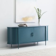 a blue sideboard with a vase on top and a painting hanging above it in a white room