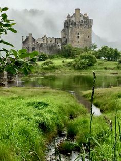 an old castle sitting on top of a lush green hillside next to a small river