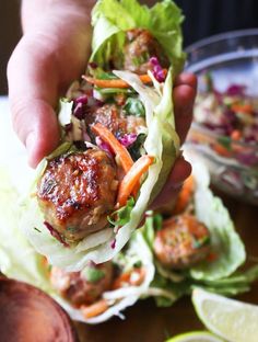 a person holding up a meatball sandwich with lettuce, carrots and slaw